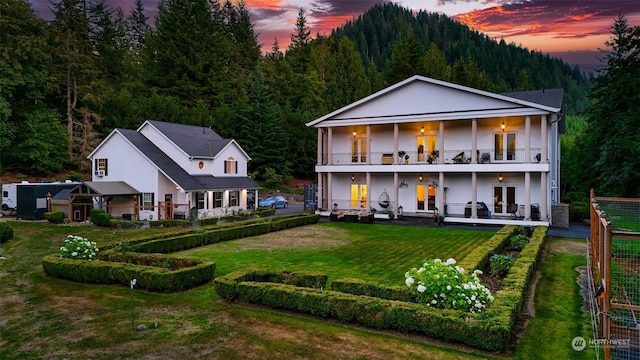 back house at dusk featuring a balcony, a patio, french doors, central AC unit, and a yard