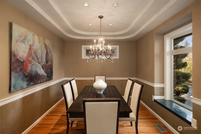 dining room with a raised ceiling, a notable chandelier, and hardwood / wood-style floors