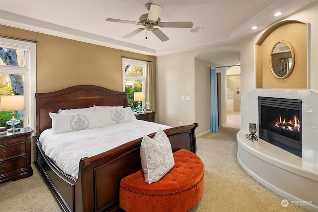 bedroom with ceiling fan, connected bathroom, light carpet, and a tray ceiling