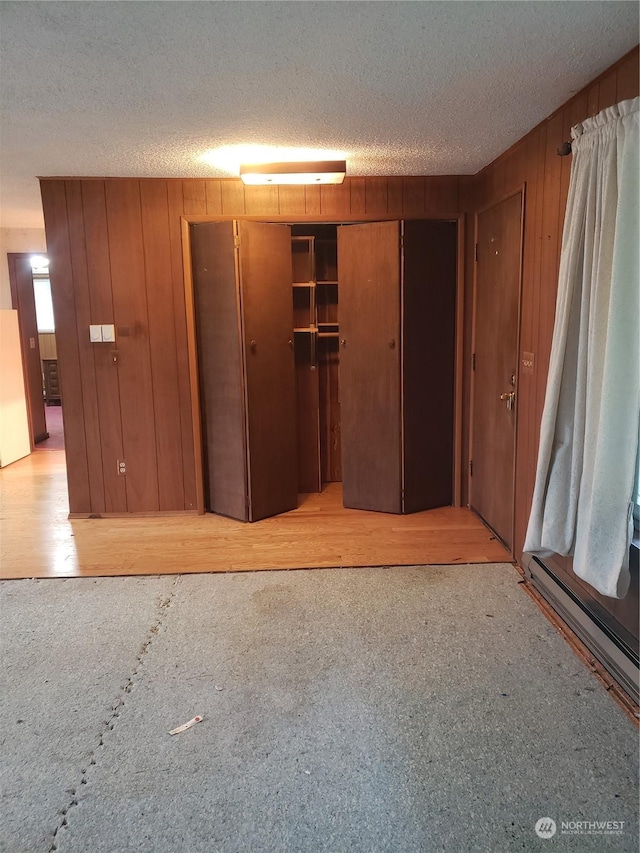 unfurnished bedroom with a textured ceiling, wooden walls, a closet, and a baseboard heating unit