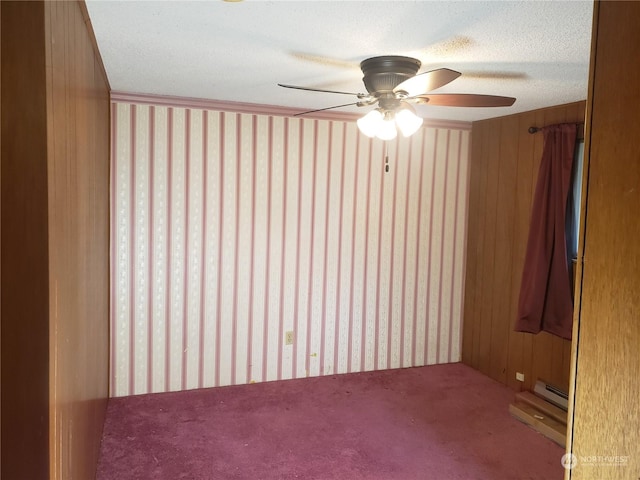 empty room featuring ceiling fan, wooden walls, baseboard heating, and a textured ceiling