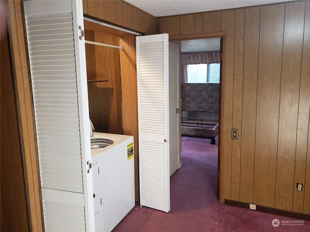 laundry area with wood walls, a textured ceiling, washer and clothes dryer, and dark carpet