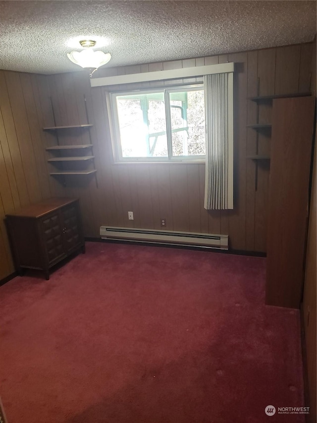 empty room featuring dark carpet, wood walls, a baseboard radiator, and a textured ceiling