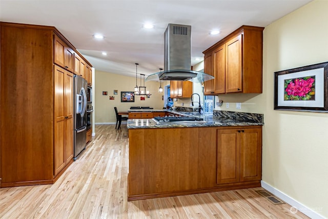 kitchen with light wood-type flooring, island exhaust hood, kitchen peninsula, hanging light fixtures, and dark stone counters