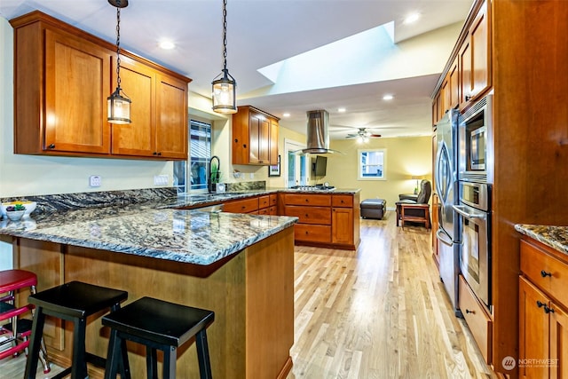 kitchen featuring decorative light fixtures, a kitchen breakfast bar, a skylight, dark stone counters, and appliances with stainless steel finishes