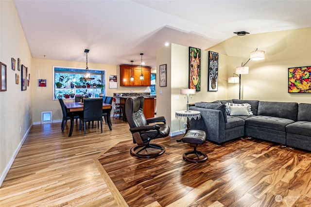 living room with lofted ceiling, light wood-type flooring, and a notable chandelier