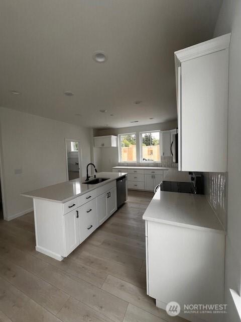 kitchen with a sink, light wood-style floors, white cabinetry, a center island with sink, and dishwashing machine