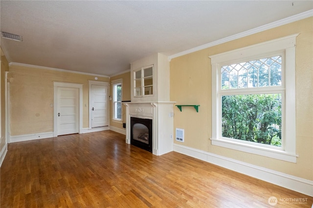 unfurnished living room with ornamental molding, visible vents, a fireplace, and wood finished floors