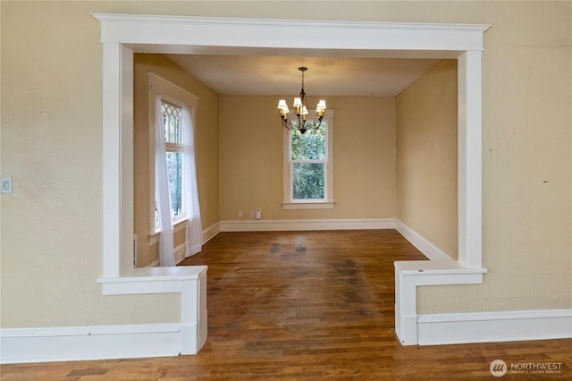 unfurnished dining area with a notable chandelier, baseboards, and wood finished floors