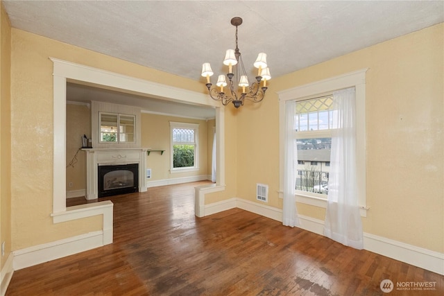 unfurnished living room featuring a notable chandelier, a fireplace, baseboards, and wood finished floors