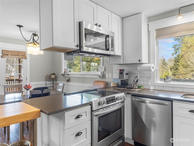 kitchen with tasteful backsplash, hanging light fixtures, white cabinets, and appliances with stainless steel finishes