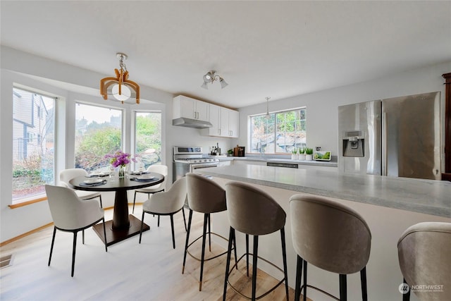 kitchen with stainless steel appliances, white cabinets, decorative light fixtures, and light hardwood / wood-style floors