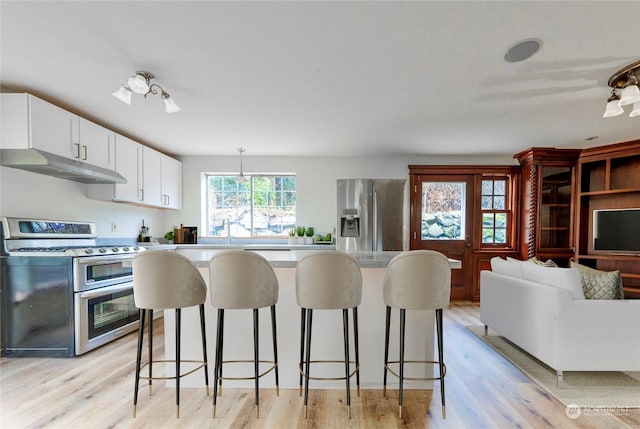 kitchen with white cabinetry, a kitchen bar, light hardwood / wood-style flooring, pendant lighting, and appliances with stainless steel finishes