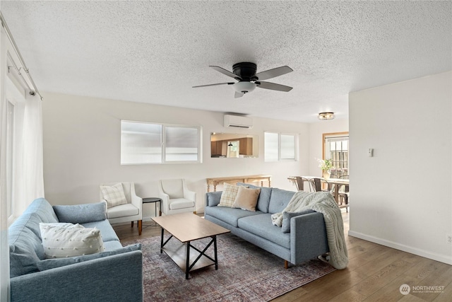 living room featuring dark wood-type flooring, a textured ceiling, ceiling fan, and a wall mounted air conditioner