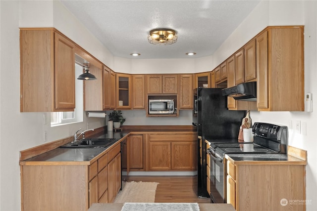 kitchen featuring black appliances, hanging light fixtures, light hardwood / wood-style floors, a textured ceiling, and sink