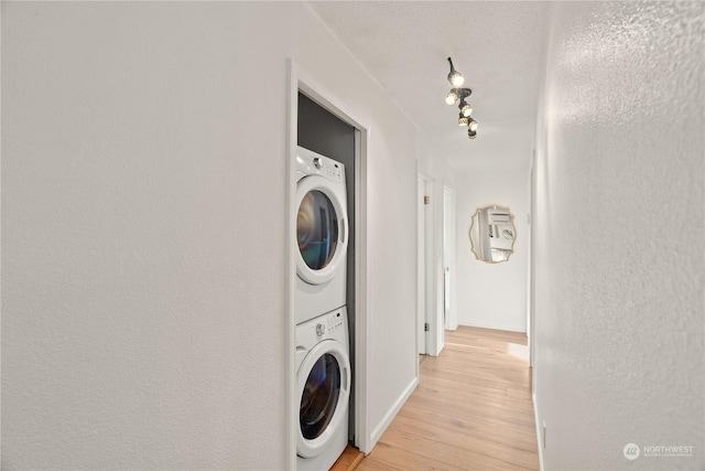 washroom with a textured ceiling, light hardwood / wood-style flooring, and stacked washer and clothes dryer