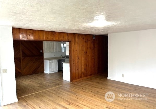 kitchen featuring black dishwasher, wooden walls, a textured ceiling, and light hardwood / wood-style floors