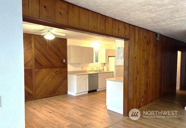 kitchen featuring sink, white cabinetry, light hardwood / wood-style flooring, stainless steel dishwasher, and wooden walls