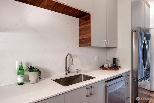 kitchen with sink, light stone countertops, dishwasher, and stainless steel fridge