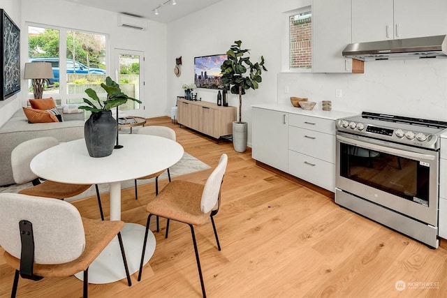 kitchen featuring an AC wall unit, electric stove, decorative backsplash, and white cabinetry