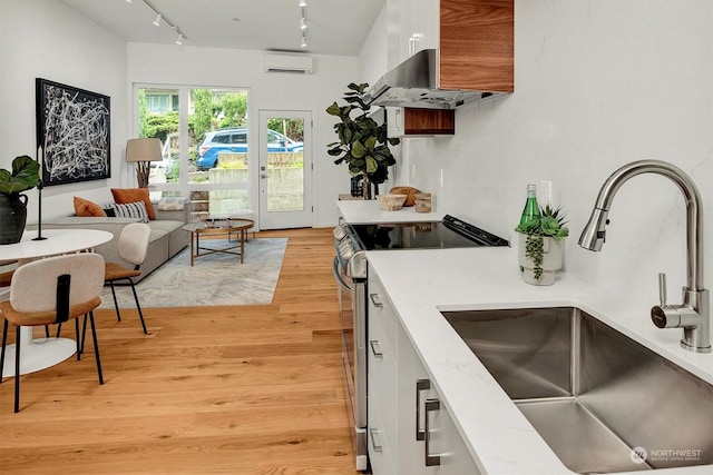 kitchen with white cabinets, electric stove, a wall unit AC, sink, and light hardwood / wood-style flooring