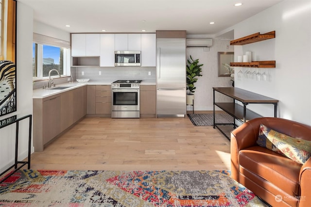 kitchen featuring appliances with stainless steel finishes, a wall mounted AC, light hardwood / wood-style floors, white cabinets, and sink