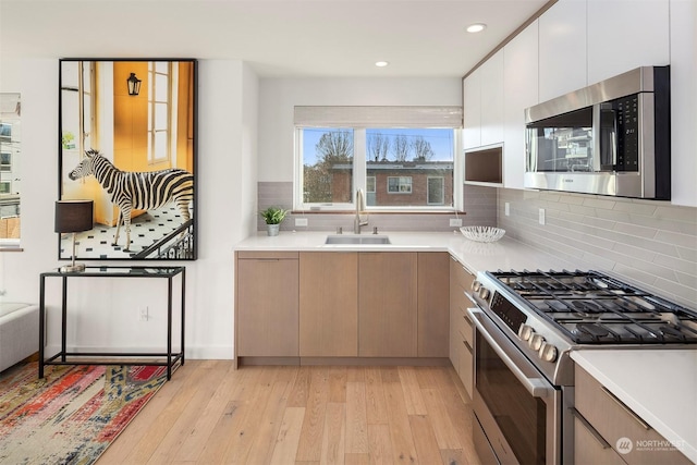 kitchen with light hardwood / wood-style flooring, stainless steel appliances, tasteful backsplash, white cabinets, and sink