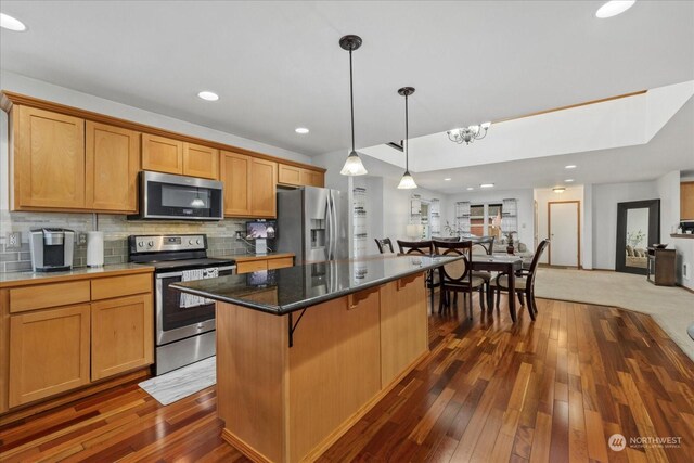 kitchen with stainless steel appliances, decorative light fixtures, backsplash, a kitchen island, and dark wood-type flooring