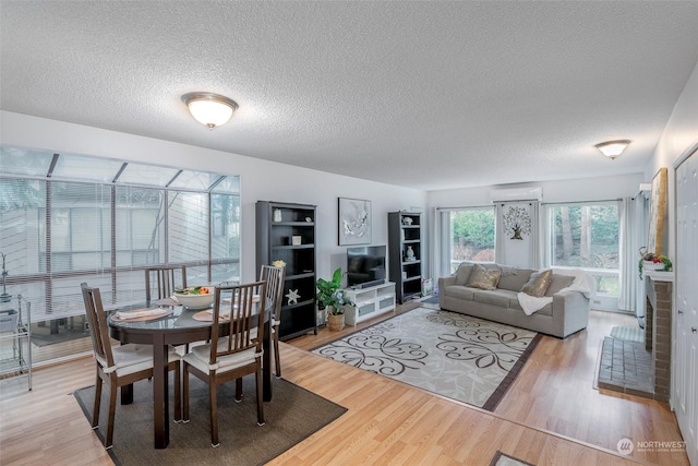 dining room featuring a textured ceiling, a wall unit AC, and light hardwood / wood-style flooring