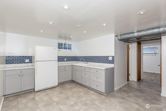 kitchen with decorative backsplash, white refrigerator, gray cabinets, and sink