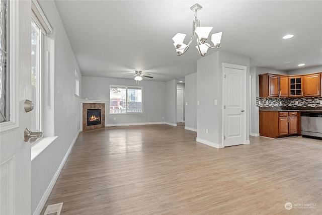 unfurnished living room with ceiling fan with notable chandelier, light hardwood / wood-style flooring, and a fireplace