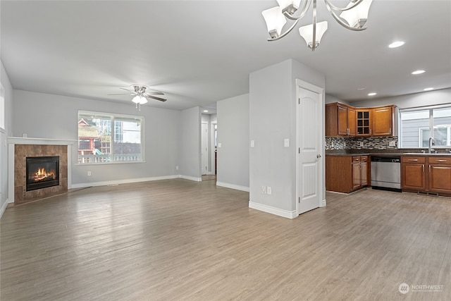 unfurnished living room featuring sink, ceiling fan with notable chandelier, light hardwood / wood-style floors, and a fireplace