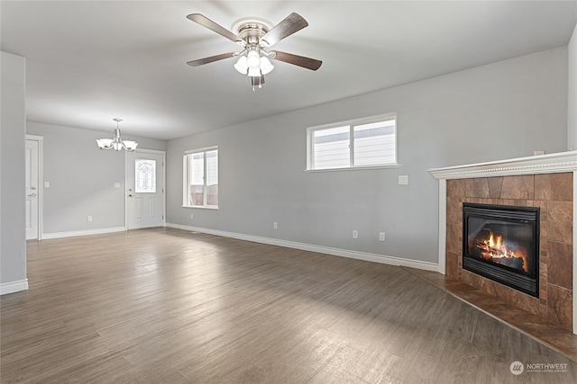 unfurnished living room with a tile fireplace, ceiling fan with notable chandelier, and dark hardwood / wood-style floors