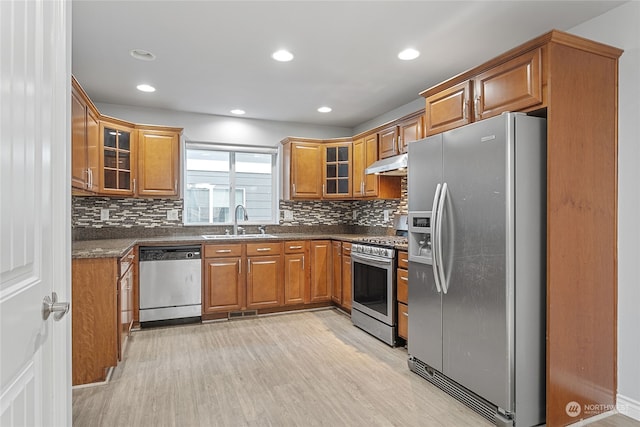 kitchen featuring appliances with stainless steel finishes, sink, light hardwood / wood-style flooring, backsplash, and dark stone counters