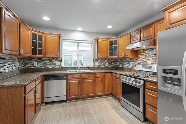 kitchen featuring appliances with stainless steel finishes, dark stone counters, tasteful backsplash, light hardwood / wood-style floors, and sink