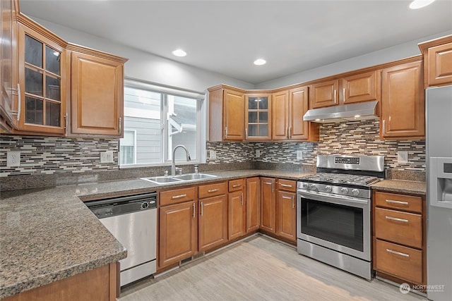 kitchen featuring appliances with stainless steel finishes, decorative backsplash, sink, light wood-type flooring, and dark stone countertops