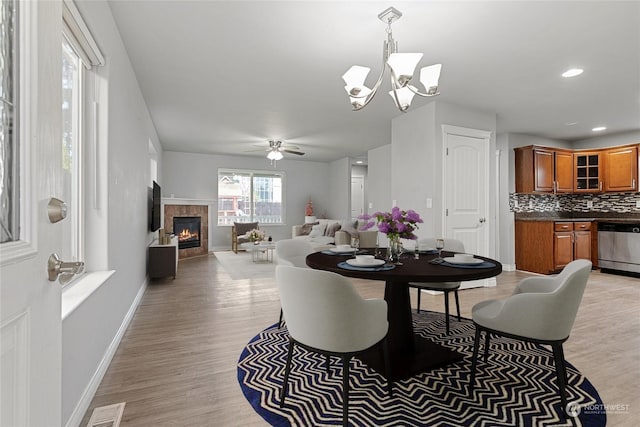 dining room featuring light hardwood / wood-style floors, ceiling fan with notable chandelier, and a fireplace