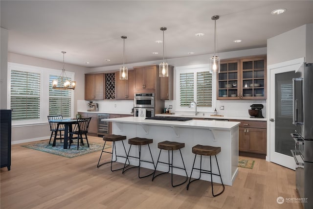 kitchen with a breakfast bar, wine cooler, hanging light fixtures, a center island, and light hardwood / wood-style floors