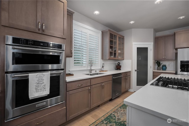 kitchen with tasteful backsplash, appliances with stainless steel finishes, sink, and light wood-type flooring