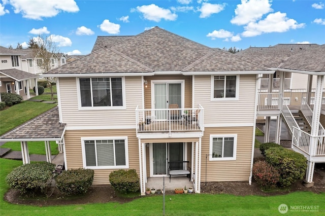 rear view of property with a balcony, a lawn, and a shingled roof