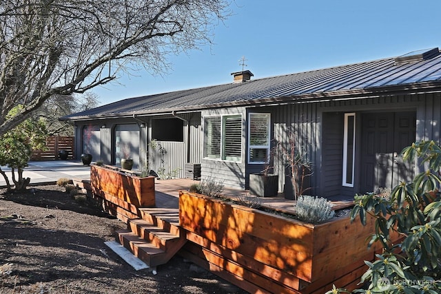 rear view of house with metal roof, driveway, board and batten siding, a standing seam roof, and a chimney