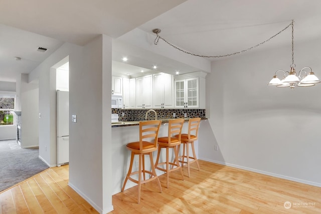 kitchen featuring white appliances, a kitchen breakfast bar, tasteful backsplash, white cabinets, and kitchen peninsula