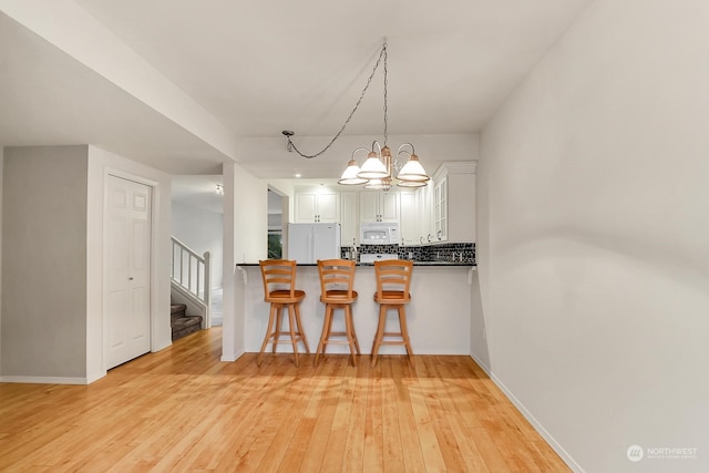 kitchen featuring tasteful backsplash, a kitchen breakfast bar, kitchen peninsula, white appliances, and white cabinets