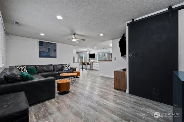 living room featuring a barn door, ceiling fan, hardwood / wood-style floors, and a textured ceiling