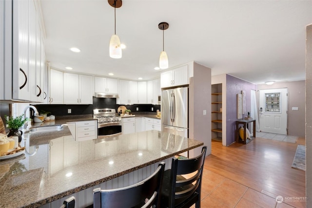 kitchen with stainless steel appliances, sink, white cabinetry, dark stone counters, and hanging light fixtures