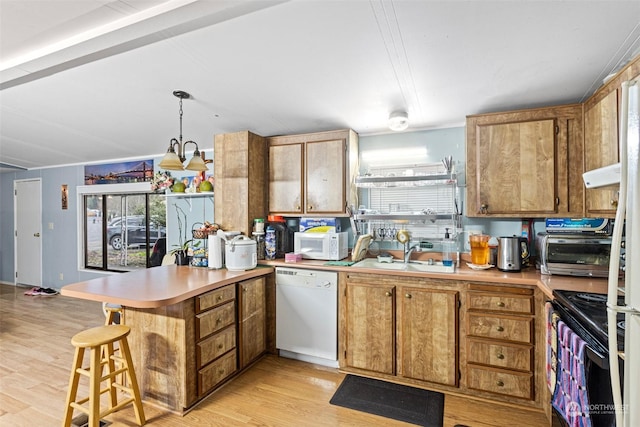 kitchen featuring white appliances, hanging light fixtures, light wood-type flooring, kitchen peninsula, and sink