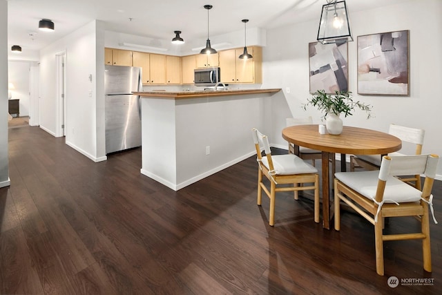 kitchen featuring pendant lighting, light brown cabinets, dark hardwood / wood-style floors, appliances with stainless steel finishes, and kitchen peninsula