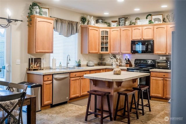 kitchen featuring light brown cabinetry, a breakfast bar, black appliances, a kitchen island, and sink