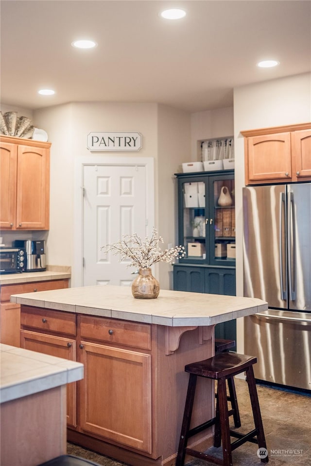 kitchen with a kitchen breakfast bar, a center island, tile countertops, and stainless steel fridge