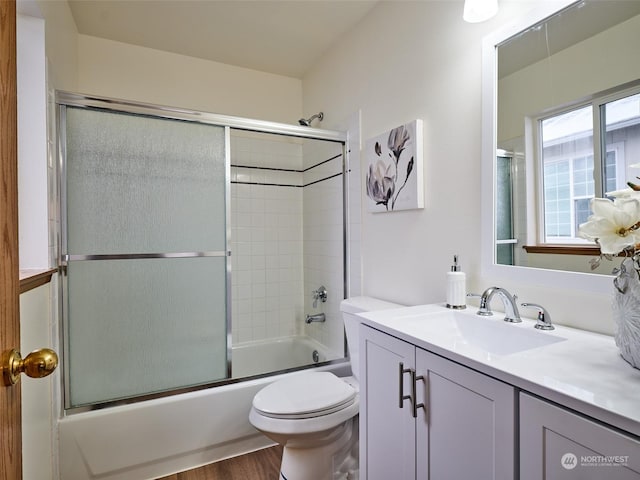 bathroom with enclosed tub / shower combo, vanity, toilet, and wood finished floors